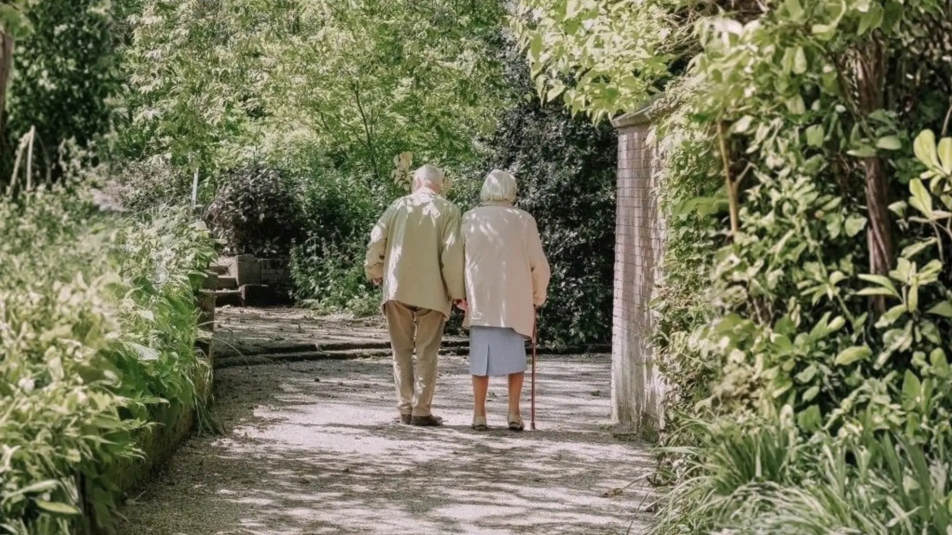 An older couple walking together down a quiet garden path